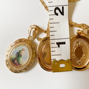 Puede incluir: Collar de cadena de oro con dos colgantes ovalados. Un colgante presenta una imagen religiosa de un hombre con ropa verde. El otro colgante est&aacute; vac&iacute;o.