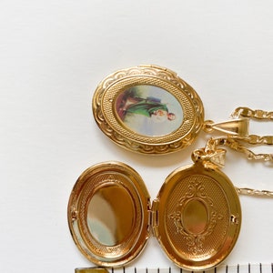 Puede incluir: Collar con dije ovalado de oro, con una imagen religiosa en la parte delantera y un dise&ntilde;o decorativo en la parte posterior. El dije est&aacute; abierto y la cadena es visible.