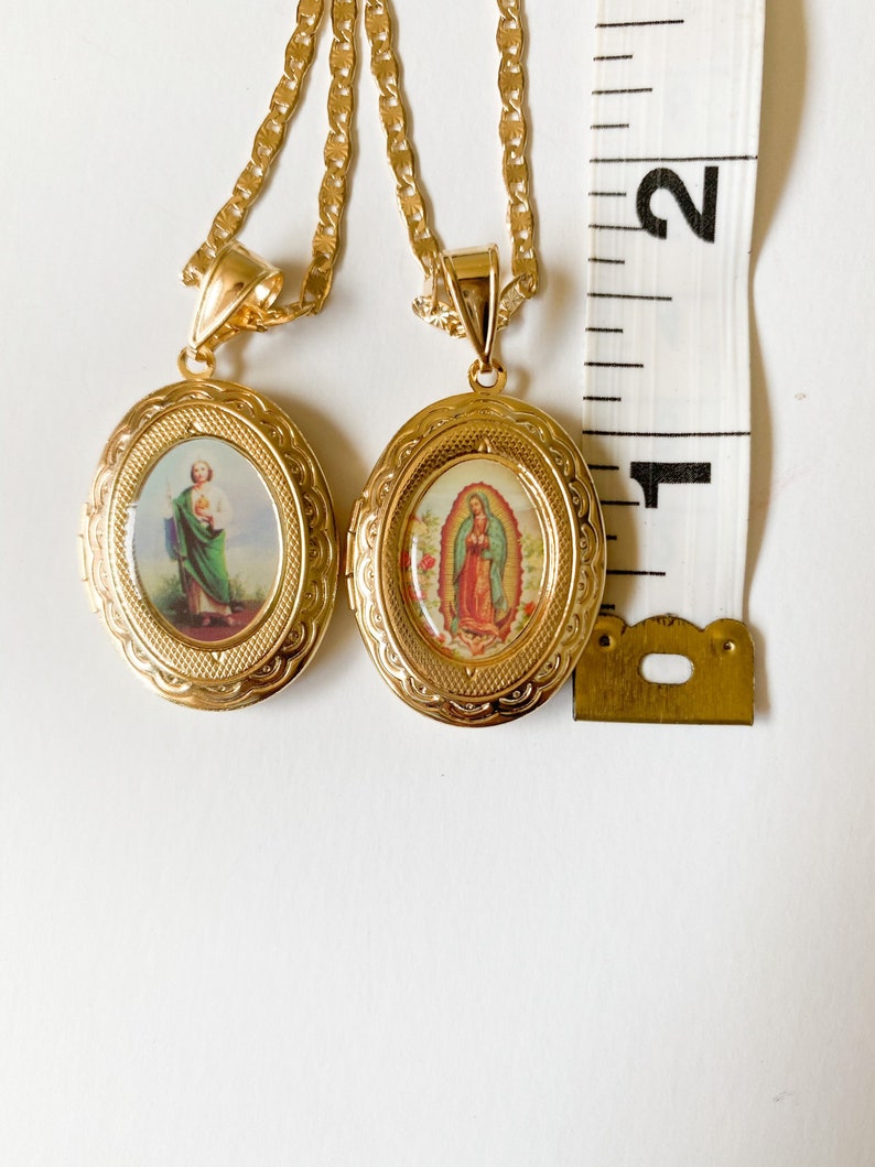Puede incluir: Dos collares de cadena de oro con medallones de forma ovalada. Los medallones presentan im&aacute;genes de figuras religiosas, una con un hombre con una t&uacute;nica verde y la otra con una mujer con una t&uacute;nica azul.