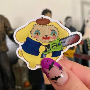 May include: A yellow cartoon dog wearing a blue jacket and a beret holds a chainsaw with a red blade. The dog has stitches on its face and is wearing makeup. The background is blurry and shows a person's hand with purple nail polish.