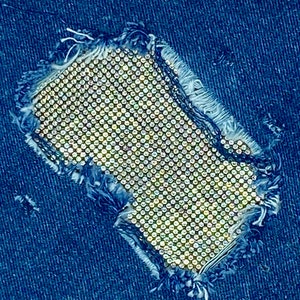 May include: A close-up of a denim fabric with a hole that is covered with a sparkly, silver-toned material. The material is made up of small, round rhinestones.