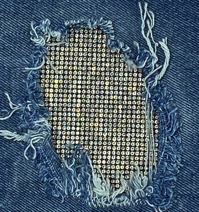 May include: A close-up of a denim fabric with a hole that has been patched with a sparkly, iridescent material. The patch is a grid of small, round, shiny objects.