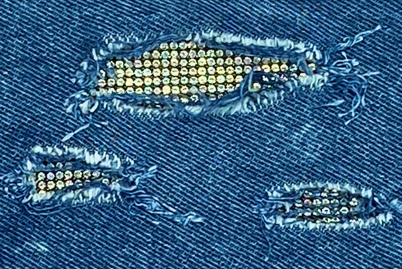 May include: Blue denim fabric with three ripped holes decorated with rows of silver rhinestones.