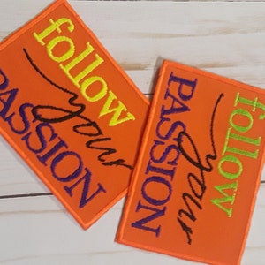 May include: Two orange rectangular patches with embroidered text. One patch reads "follow your PASSION" in yellow, black, and purple. The other patch reads "FOLLOW your PASSION" in green, black, and purple. Both patches have an orange border.