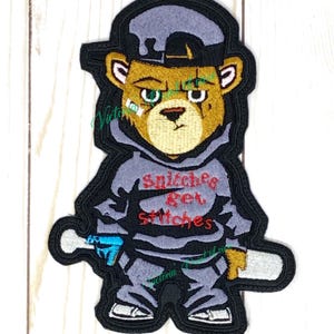 May include: Embroidered iron-on patch featuring a cartoon bear wearing a grey hoodie, a black baseball cap, and holding a blue and white spray can and a white baseball bat. The bear's hoodie has the text "Snitches Get Stitches" in red.