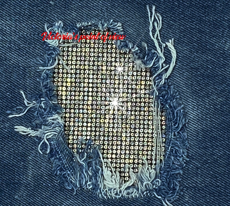 May include: A close-up of a denim fabric with a large hole that has been patched with a grid of clear rhinestones.