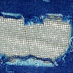 May include: A close-up of a blue denim fabric with a hole that has been patched with a silver sequined fabric.