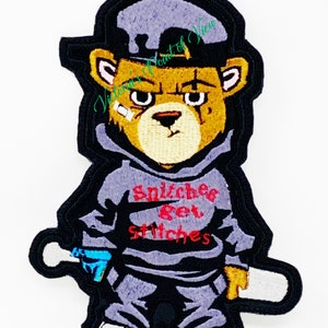 Puede incluir: Un parche bordado para planchar que presenta un oso de dibujos animados con una sudadera gris, pantalones negros, una gorra de b&eacute;isbol negra y sosteniendo un bate de b&eacute;isbol blanco. El oso tiene una expresi&oacute;n gru&ntilde;ona y la sudadera tiene el texto "Snitchers Get Stitches" en rojo.