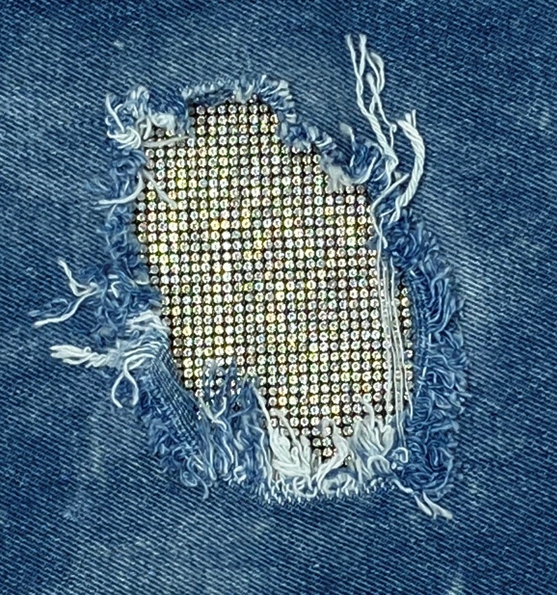 May include: A close-up of a denim fabric with a hole that has been patched with a grid of rhinestones.