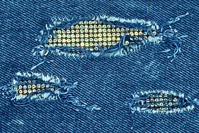 May include: Blue denim fabric with three ripped holes decorated with rows of silver rhinestones.