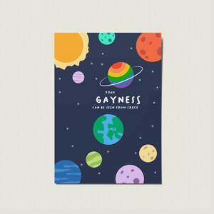 May include: A navy blue print featuring a cartoon solar system with planets and stars. The central planet is a rainbow-colored sphere with a ring. The text reads "YOUR GAYNESS CAN BE SEEN FROM SPACE."