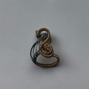 May include: A silver and gold wire ring with a unique, abstract design. The ring is made of two different colored wires that are intertwined to create a swirling pattern.