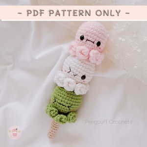Może przedstawiać: Pluszowa zabawka amigurumi w kształcie japońskiego lodu mochi na patyku. Zabawka jest wykonana z zielonej, białej i różowej przędzy i ma uroczą buźkę. Zabawka znajduje się na białym tle.  TYLKO WZÓR PDF.