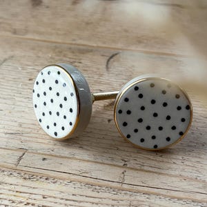 May include: Two white ceramic cabinet knobs with a gold rim and black polka dots.