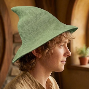 May include: A sage green knit hat with a pointed, slightly curved crown and a wide, flexible brim. The hat features a fine, horizontal ribbed texture throughout the fabric, creating a structured yet soft appearance that sits comfortably on the head.