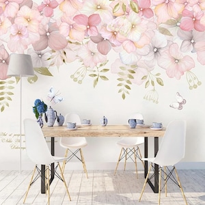 Könnte beinhalten: Eine Aquarell-Blumen-Tapete mit rosa und weißen Blüten und grünen Blättern. Die Tapete hängt an einer weißen Wand in einem Esszimmer mit einem Holztisch und vier weißen Stühlen.