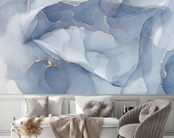 May include: A living room interior with a white couch and a gray armchair. The wall behind the couch is decorated with a blue and gold abstract art print. The couch has a brown throw blanket and two gray pillows. The armchair has a gray pillow.