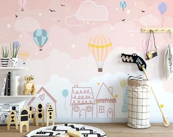 Könnte beinhalten: Ein rosa-weißes Kinderzimmer-Wandbild mit einem verspielten Design mit Heißluftballons, Wolken und Sternen. Das Wandbild enthält auch eine handgezeichnete Szene von Häusern mit Herzen und Sternen.