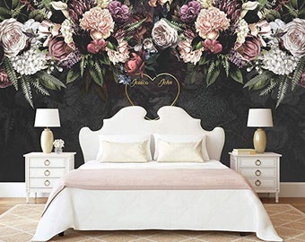 Peut inclure: Un lit blanc avec une couette rose et une tête de lit blanche. La tête de lit est ornée d'un cœur doré avec les noms "Jessica" et "John" inscrits à l'intérieur. Le lit est placé devant un mur noir orné d'une fresque florale.