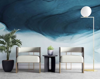 May include: Two white chairs with gold metal legs and a black side table in front of a blue and white abstract wall with a gold floor lamp with a white orb shade.