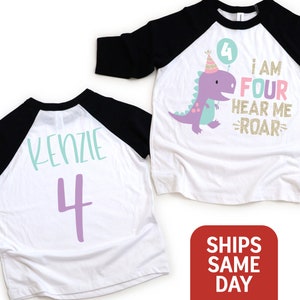 May include: White and black baseball tee shirt with a purple dinosaur graphic and the text "I am four hear me roar". The back of the shirt has the name "Kenzie" and the number "4" in purple.