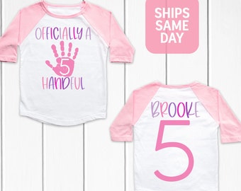May include: Two white and pink baseball style shirts with a pink handprint and the text "Officially a 5 Handful" on one shirt and the text "Brooke 5" on the other shirt.