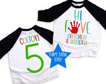 May include: Two white and black baseball shirts. One shirt says "Hi Five Officially A Handful" with a red handprint. The other shirt says "Colton 5" with a green number 5. A blue star with the text "Ships Same Day" is in the image.