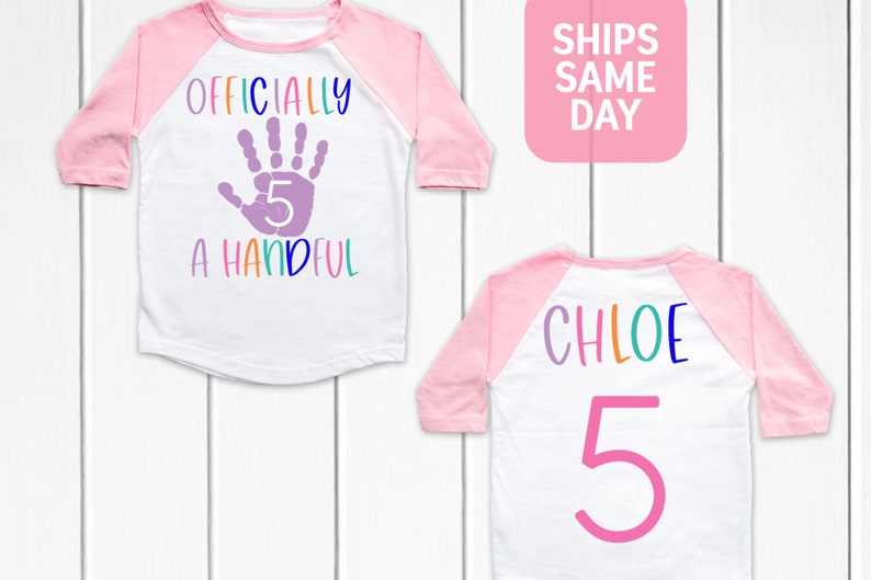 Pu&ograve; includere: Due magliette in stile baseball rosa e bianche. Una maglietta ha un'impronta di mano viola con il numero 5 all'interno e il testo "Ufficialmente una manciata". L'altra maglietta ha il nome "Chloe" in colori arcobaleno e il numero 5 in rosa.