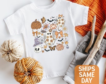 May include: White t-shirt with a colorful Halloween-themed design featuring ghosts, pumpkins, bats, and flowers. The design is centered on the shirt and includes the text "SHIPS SAME DAY".