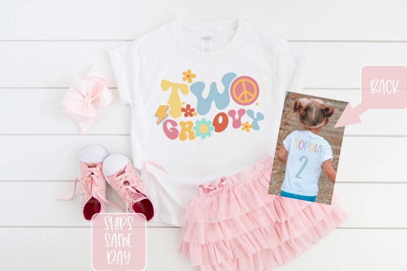 May include: A white t-shirt with the words "TWO GROOVY" in colorful retro font, a peace sign, and flower graphics. The shirt is paired with a pink tutu skirt and pink sneakers. A photo shows the back of a shirt with the name "SOPHIA" and the number "2".