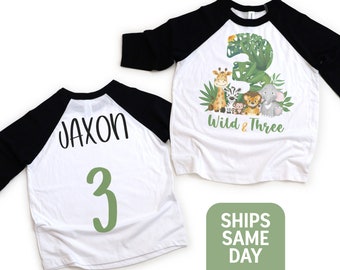 May include: White and black baseball tee shirt with green number 3 and the name Jaxon on the back. The front of the shirt has a green number 3 with jungle animals and the text "Wild & Three".