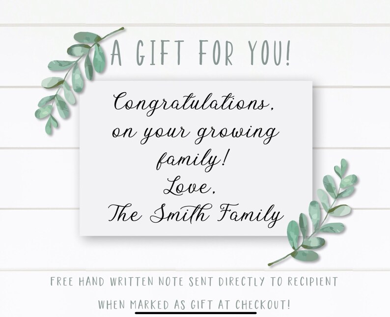 May include: A white card with a handwritten message that reads "A Gift For You! Congratulations, on your growing family! Love, The Smith Family". The card is surrounded by green leafy branches.