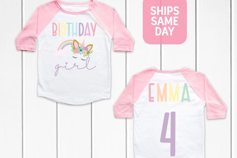 K&ouml;nnte beinhalten: Wei&szlig;es und rosafarbenes Baseball-Shirt mit einem Regenbogen-Einhorn und dem Text "Birthday girl". Auf der R&uuml;ckseite des Shirts steht der Name "Emma" in Regenbogenfarben und die Zahl "4" in Lila.