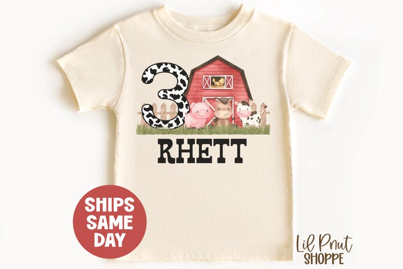 May include: A white t-shirt with a red barn, a cow, a pig, and a number 3 with black and white cow spots. The text "Rhett" is printed below the barn.