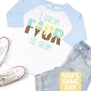 May include: White and light blue raglan t-shirt with the text "I scream four ice cream" in colorful letters that are decorated with ice cream cones. The letters are decorated with sprinkles and waffle cone patterns.