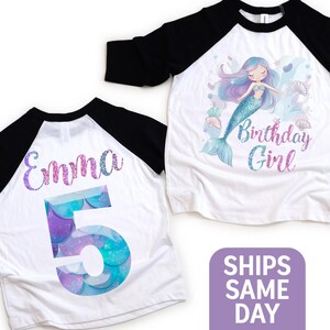 May include: White and black raglan-style birthday shirts. One shirt features a mermaid illustration with the text "Birthday Girl". The other shirt has the name "Emma" and the number "5" in a mermaid scale design.