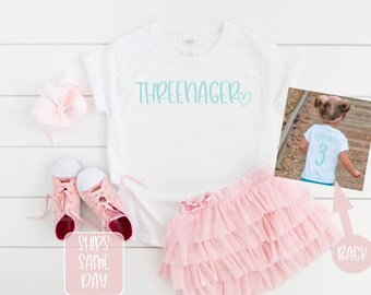 May include: White t-shirt with the text "THREE-NAGER" in teal blue with a small heart. The back of the shirt has a teal blue number "3".