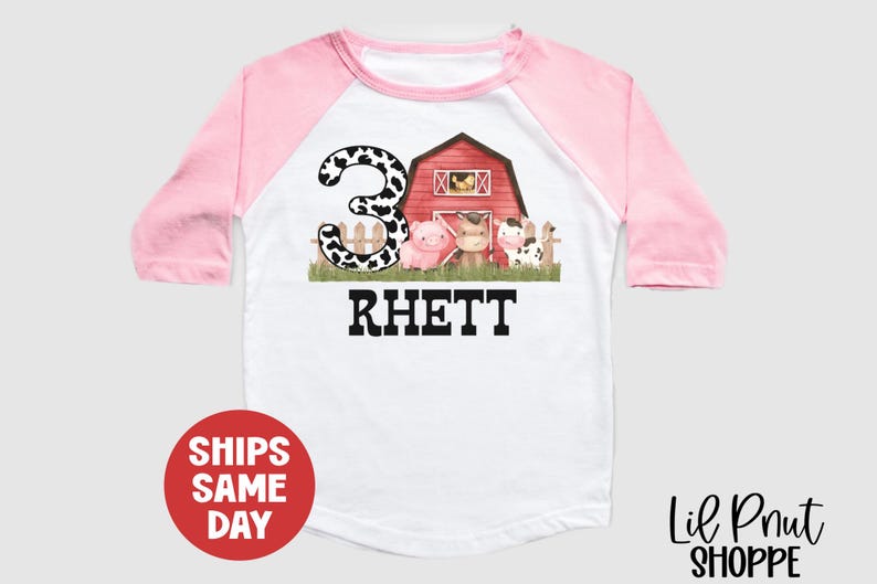 May include: A pink and white baseball style t-shirt with a cow print number 3, a red barn, and a pig, cow, and horse. The text "Rhett" is below the image.