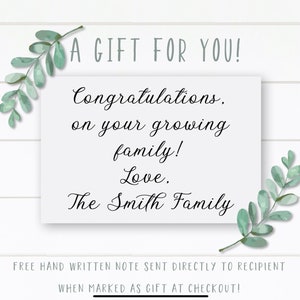 May include: A white card with a handwritten message that reads "A GIFT FOR YOU! Congratulations, on your growing family! Love. The Smith Family". The card is surrounded by green leafy branches.