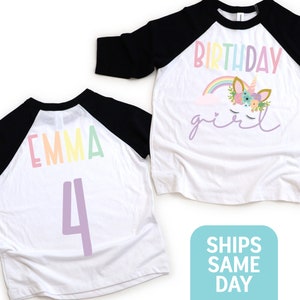 K&ouml;nnte beinhalten: Zwei wei&szlig;e und schwarze Baseball-Shirts mit Regenbogen-Schriftzug. Ein Shirt sagt "Birthday girl" mit einem Einhorn-Motiv. Das andere Shirt sagt "Emma 4".