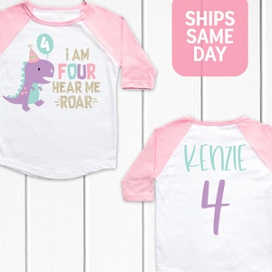 May include: A white and pink baseball style shirt with a purple dinosaur graphic and the text "I am four hear me roar" on the front. The back of the shirt has the name "Kenzie" and the number "4" in purple.