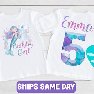 May include: Two white t-shirts with mermaid-themed designs. One shirt features a mermaid illustration with the text "Birthday Girl." The other shirt displays the name "Emma" and the number "5" in a mermaid scale pattern. A teal heart-shaped graphic is also present.