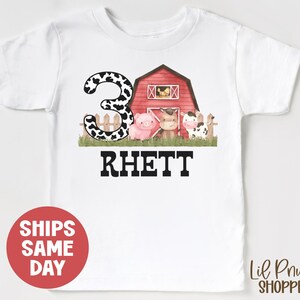 May include: White t-shirt with a black and white cow print number 3, a red barn with a pig and cow inside, and the name "Rhett" in black text.