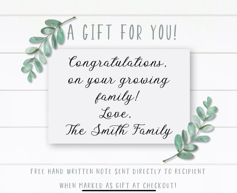 May include: A white card with a handwritten message that reads "A Gift For You! Congratulations, on your growing family! Love, The Smith Family". The card is surrounded by green leafy branches.