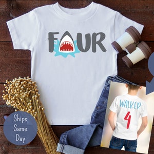 May include: White t-shirt with a gray "FOUR" graphic featuring a shark with red teeth and blue water splatter. The back of the shirt has a red "4" and the name "WALKER" in blue.