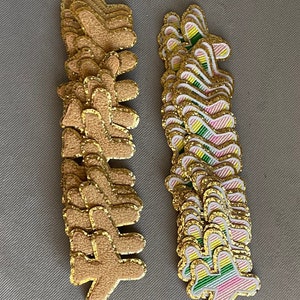 May include: Two stacks of gold glitter iron-on patches. One stack has 12 brown patches shaped like a hand with a gold glitter outline. The other stack has 12 pink, green, and yellow striped patches shaped like a hand with a gold glitter outline.