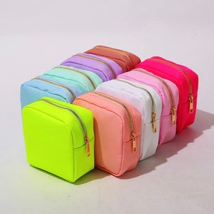 May include: A set of ten small zippered pouches in various pastel colors, including pink, blue, green, yellow, and white. The pouches are made of a soft, textured fabric and have gold zippers.