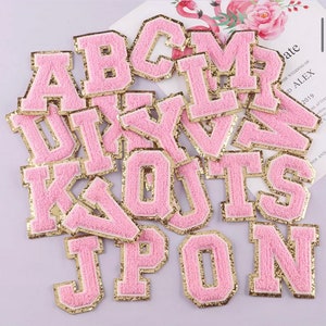 May include: A set of pink felt letters with gold trim. The letters are in uppercase and include A, B, C, D, I, J, K, L, M, N, O, P, Q, R, S, T, U, V, W, X, Y, and Z.