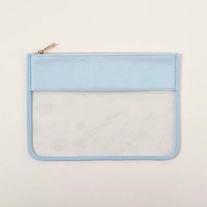 May include: A light blue zippered pouch with a clear plastic window. The pouch is made of a soft, textured material.
