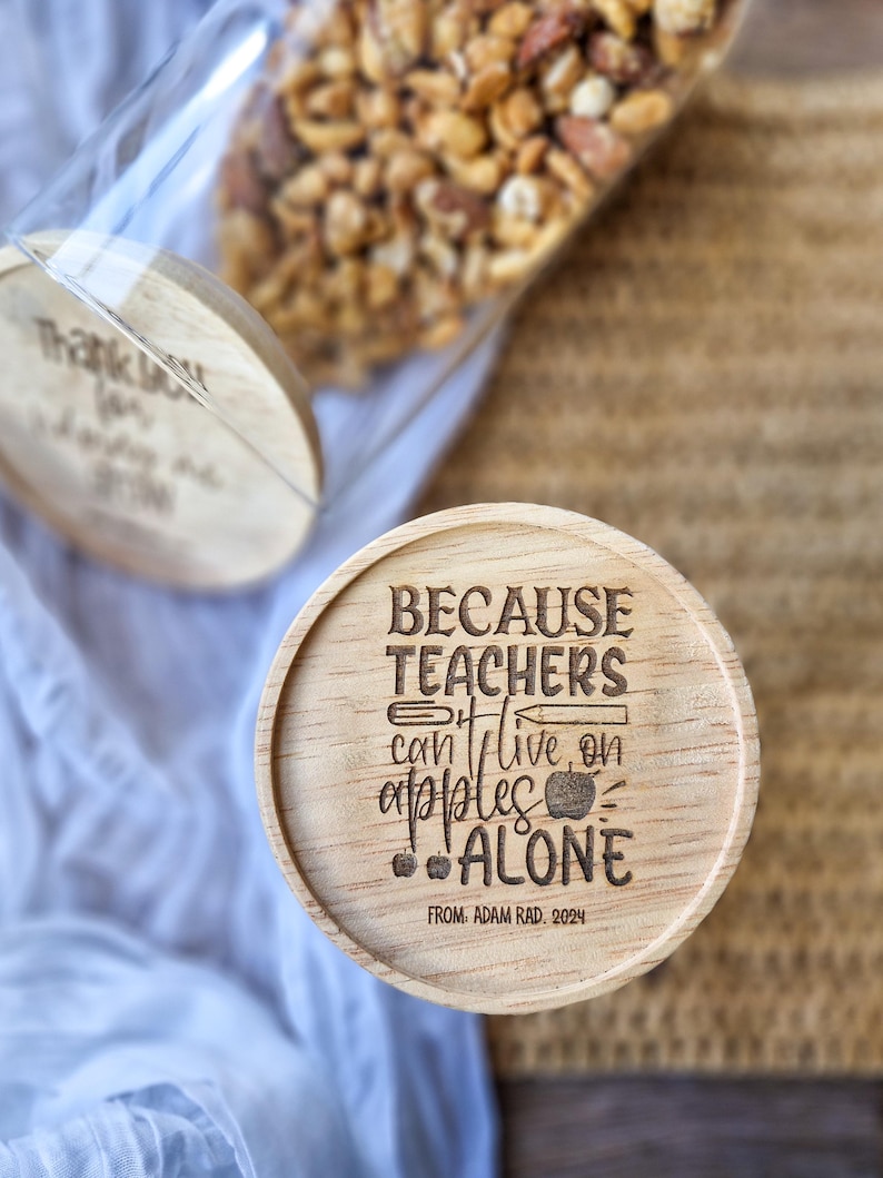 May include: Wooden jar lid with the text "Because teachers can't live on apples alone" and the text "From Adam Rad. 2024".